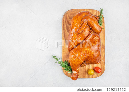 A roasted spatchcocked chicken on a wooden board garnished with rosemary and cherry tomatoes on a light background, top view. copy space. 129215532