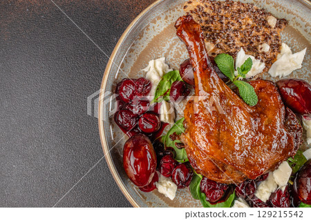 A glazed roasted duck leg on a ceramic plate with cherry compote, creamy cheese, arugula, and a crispy seed cracker. top view. copy space A glazed roasted duck leg on a ceramic plate with cherry compote, creamy cheese, arugula, and a crispy seed cracker. top view. copy space 129215542