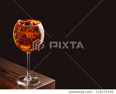 A cocktail with ice served in a large stemmed glass on a dark wooden bar with a black background. copy space for text 129215548
