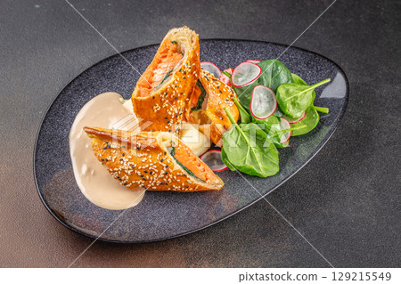 Salmon Wellington with mashed potatoes, spinach-radish salad, and creamy sauce on a black ceramic plate. top view Salmon Wellington with mashed potatoes, spinach-radish salad, and creamy sauce on a black ceramic plate. top view 129215549