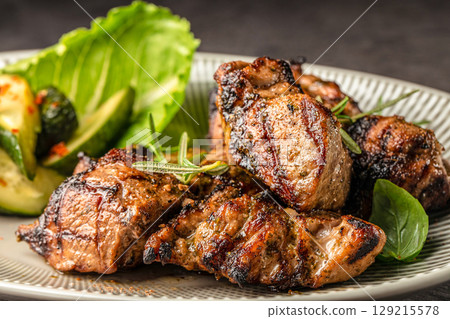 Grilled marinated pork pieces served with fresh greens and roasted zucchini on a ceramic plate Grilled marinated pork pieces served with fresh greens and roasted zucchini on a ceramic plate 129215578