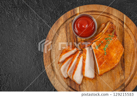 A sliced grilled pork chop on a wooden board with ketchup and fresh thyme garnish. top view. copy space. 129215583