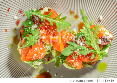 Toasted bread topped with fresh arugula, avocado spread, smoked salmon, olives, and grated cheese for a vibrant and savory appetizer. top view 129215616