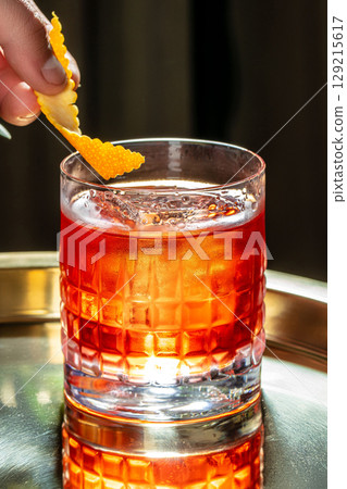 A classic cocktail served in a textured glass with a vibrant orange twist garnish, capturing a moment of refined elegance and refreshment. copy space 129215617