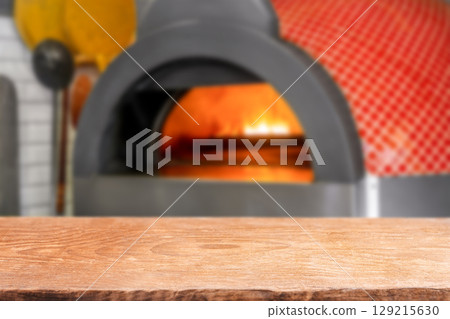 Empty wooden table in front of a traditional pizza oven with fire glowing inside Empty wooden table in front of a traditional pizza oven with fire glowing inside 129215630