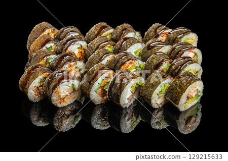 A large assortment of nori-wrapped sushi rolls filled with fish, vegetables, and drizzled with dark savory sauce, displayed on a glossy black surface A large assortment of nori-wrapped sushi rolls filled with fish, vegetables, and drizzled with dark savory sauce, displayed on a glossy black surface 129215633