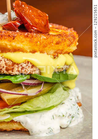 Layered gourmet burger with crispy potato patties, creamy sauces, pickles, lettuce, spinach, onions, and sundried tomato on top Layered gourmet burger with crispy potato patties, creamy sauces, pickles, lettuce, spinach, onions, and sundried tomato on top 129215651