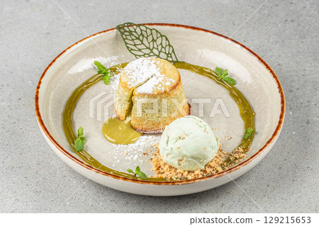 Matcha molten lava cake with a dusting of powdered sugar, paired with a scoop of pistachio ice cream and garnished with mint and crushed nuts on a decorative plate Matcha molten lava cake with a dusting of powdered sugar, paired with a scoop of pistachio ice cream and garnished with mint and crushed nuts on a decorative plate 129215653