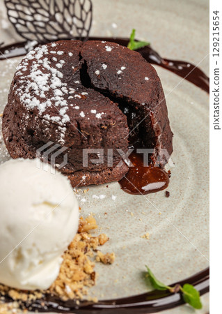 Classic chocolate lava cake with a rich molten center, dusted with powdered sugar and served with a scoop of vanilla ice cream and crumbled nuts 129215654
