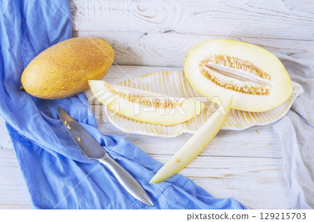 Cut ripe melon. Melon and knife on white wooden background. Top view. Beautiful still life. Cut ripe melon. Melon and knife on white wooden background. Top view. Beautiful still life. 129215703