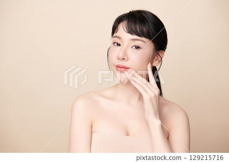 A beautiful young Asian woman with clean, fresh skin against a beige background. Skincare, facial treatment, cosmetology, beauty, and spa. An elegant portrait of an Asian woman. 129215716