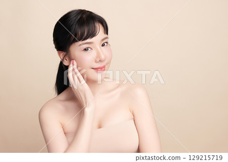A beautiful young Asian woman with clean, fresh skin against a beige background. Skincare, facial treatment, cosmetology, beauty, and spa. An elegant portrait of an Asian woman. 129215719