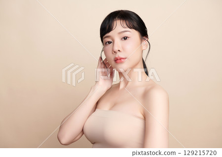 A beautiful young Asian woman with clean, fresh skin against a beige background. Skincare, facial treatment, cosmetology, beauty, and spa. An elegant portrait of an Asian woman. 129215720
