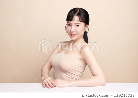 A beautiful young Asian woman with clean, fresh skin against a beige background. Skincare, facial treatment, cosmetology, beauty, and spa. An elegant portrait of an Asian woman. 129215722