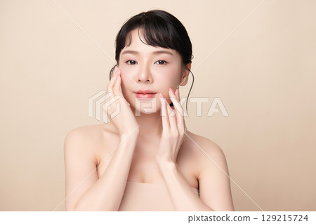 A beautiful young Asian woman with clean, fresh skin against a beige background. Skincare, facial treatment, cosmetology, beauty, and spa. An elegant portrait of an Asian woman. 129215724