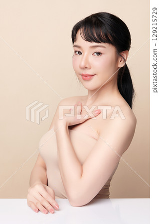A beautiful young Asian woman with clean, fresh skin against a beige background. Skincare, facial treatment, cosmetology, beauty, and spa. An elegant portrait of an Asian woman. A beautiful young Asian woman with clean, fresh skin against a beige background. Skincare, facial treatment, cosmetology, beauty, and spa. An elegant portrait of an Asian woman. 129215729