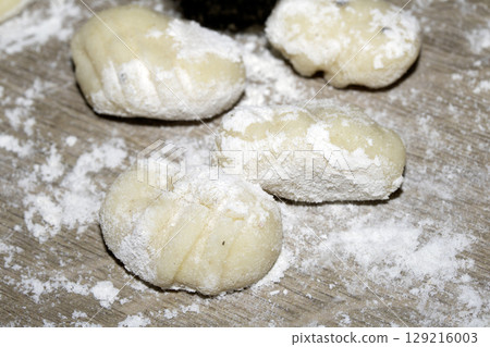 Close up of gnocchi pasta beinng made raw on wooden background covered in flour 129216003