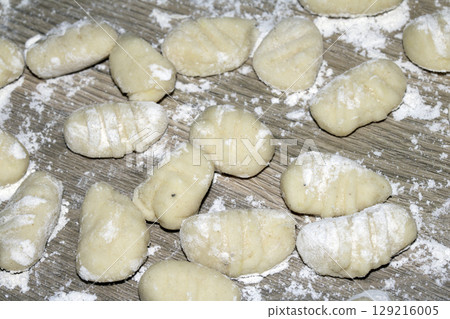 Close up of gnocchi pasta beinng made raw on wooden background covered in flour Close up of gnocchi pasta beinng made raw on wooden background covered in flour 129216005