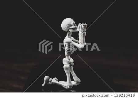 Pray skeleton figurine. Prayer figure on knees on dark background 129216419