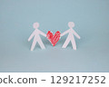 On a blue background, a paper couple holds a red paper heart in their hands. The concept of love, caring, family, and help 129217252
