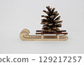 There is a brown pine cone on a white background on a wooden sled. 129217257