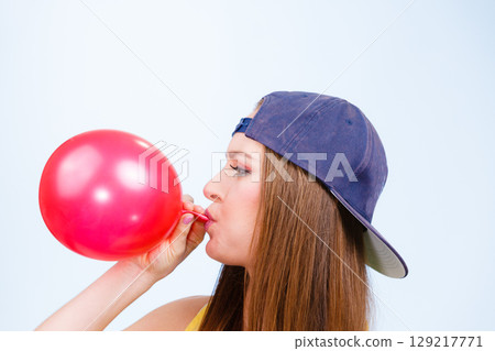 Teen girl blowing red balloon. 129217771