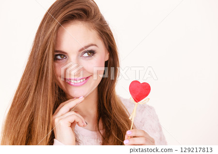 Flirty woman holding red wooden heart on stick Flirty woman holding red wooden heart on stick 129217813