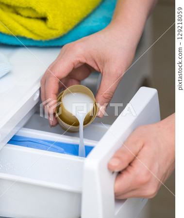 Person pouring fabric softener into washing machine 129218059