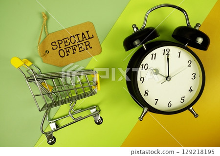 Special Offer text on price tag with alarm clock and trolley shopping cart on green, yellow geometric background 129218195