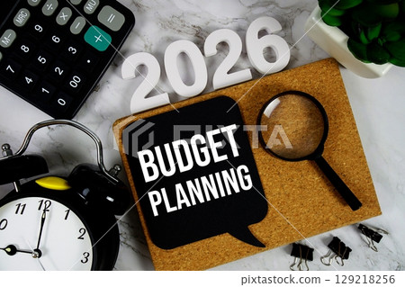 Budget Planning 2026 text message with calculator, alarm clock and magnifying glass on wooden background 129218256