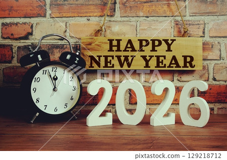 Happy New Year 2026 letters with alarm clock on wooden background Happy New Year 2026 letters with alarm clock on wooden background 129218712