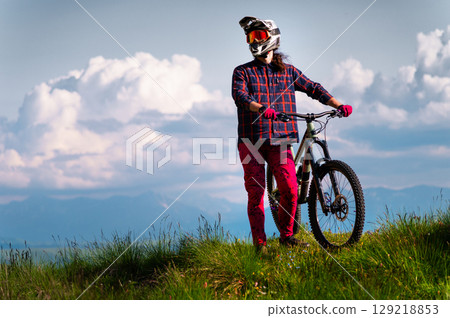 Portrait of a cyclist standing with his bicycle against a dramatic sky with cumulus clouds. Handsome young man biking in the countryside Portrait of a cyclist standing with his bicycle against a dramatic sky with cumulus clouds. Handsome young man biking in the countryside 129218853