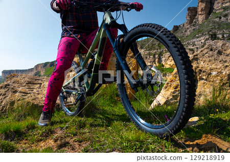 Close-up view of the legs of an unrecognizable rider and the pedals of a bicycle from below. A man in brightly colored clothing stands on a bicycle in the mountains Close-up view of the legs of an unrecognizable rider and the pedals of a bicycle from below. A man in brightly colored clothing stands on a bicycle in the mountains 129218919