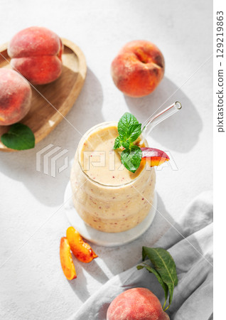 Smoothie with peach and banana in a glass on a marble stand on a light background 129219863