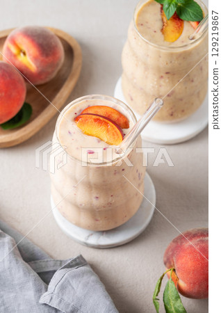 Two glasses of smoothie with peach and banana in a glass on a light background with tropical fruits 129219867
