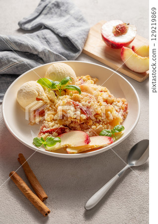 Peach crumble or cobbler with vanilla ice cream scoops and cinnamon on a plate on a light background 129219869
