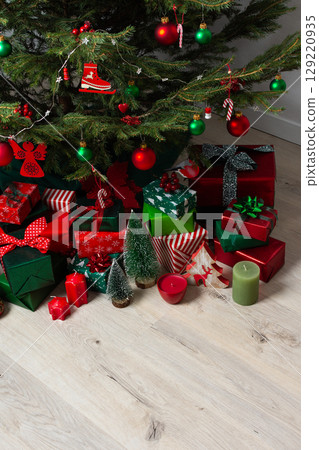 A festive display of green and red gift boxes under a beautifully decorated Christmas tree, complemented by candles and traditional ornaments, evoking warmth and holiday cheer 129220935