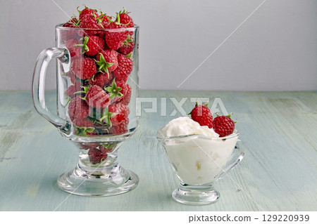 sweet ripe raspberries in a glass and a cup with cream. 129220939