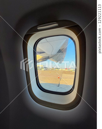 View through airplane window showing engine and runway during boarding. Travel experience, perspective, and anticipation before takeoff. View through airplane window showing engine and runway during boarding. Travel experience, perspective, and anticipation before takeoff. 129221113