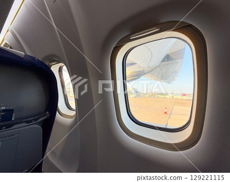 Interior view from airplane seat with engine and runway outside. Travel atmosphere, pre-flight waiting, and onboard passenger perspective. Interior view from airplane seat with engine and runway outside. Travel atmosphere, pre-flight waiting, and onboard passenger perspective. 129221115