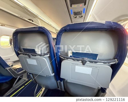 Airplane interior showing back of seats and cabin lighting. Travel routine, onboard details, and passenger environment during flight preparation. 129221116