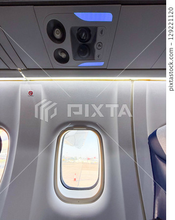 Airplane window view with visible engine and control panel above. Passenger environment, aviation design, and inflight atmosphere before departure. 129221120