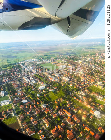 Aerial view of town and countryside from airplane window with engine visible. Urban planning, landscape diversity, and in-flight travel perspective. 129221125