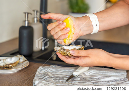 Freshly opened oyster held in hands and sprinkled with lemon juice. Homemade seafood preparation before eating Freshly opened oyster held in hands and sprinkled with lemon juice. Homemade seafood preparation before eating 129221308