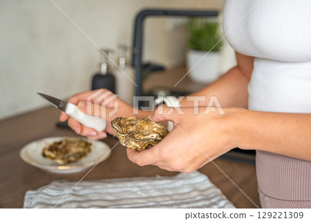 Female hands struggling to open a fresh oyster at home with a special oyster knife. Risks and challenges of handling shellfish without professional training Female hands struggling to open a fresh oyster at home with a special oyster knife. Risks and challenges of handling shellfish without professional training 129221309