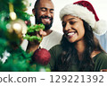 Christmas, tree and smile with a black couple decorating in the home together for the festive season. Love, celebration and holidays with a happy man and woman in a santa hat while bonding in a house 129221392