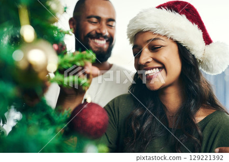 Christmas, tree and smile with a black couple decorating in the home together for the festive season. Love, celebration and holidays with a happy man and woman in a santa hat while bonding in a house 129221392