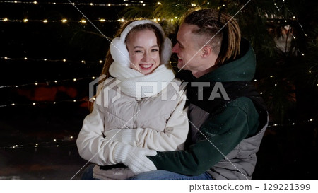 Affectionate couple hugging, sharing warmth under twinkling string lights, surrounded by gently falling snow on crisp winter evening during holiday season Affectionate couple hugging, sharing warmth under twinkling string lights, surrounded by gently falling snow on crisp winter evening during holiday season 129221399