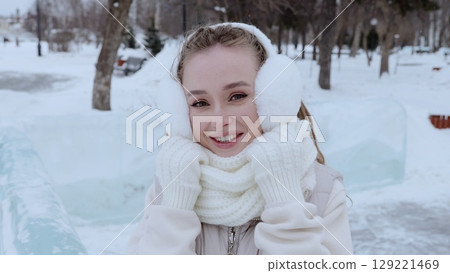 Young woman bundled in winter attire, smiling brightly while walking through snow covered park, radiating joy amid frosty landscape Young woman bundled in winter attire, smiling brightly while walking through snow covered park, radiating joy amid frosty landscape 129221469