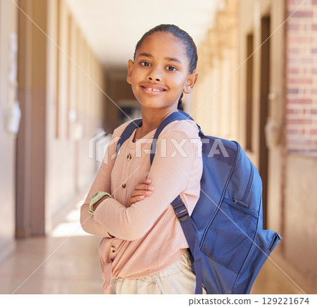 Backpack, happy and portrait of a girl at school in the hallway for education, scholarship and learning. Happiness, study and child student with smile standing at academy with bag for back to school. Backpack, happy and portrait of a girl at school in the hallway for education, scholarship and learning. Happiness, study and child student with smile standing at academy with bag for back to school. 129221674
